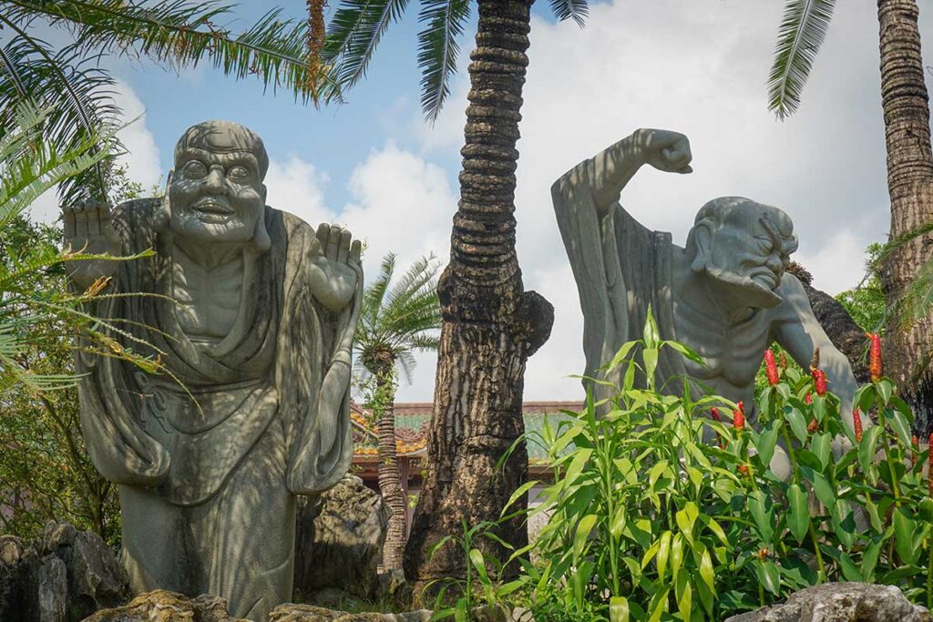Stone Arhat statues at Thien Hung Pagoda in Binh Dinh, Vietnam, set among palm trees and gardens.