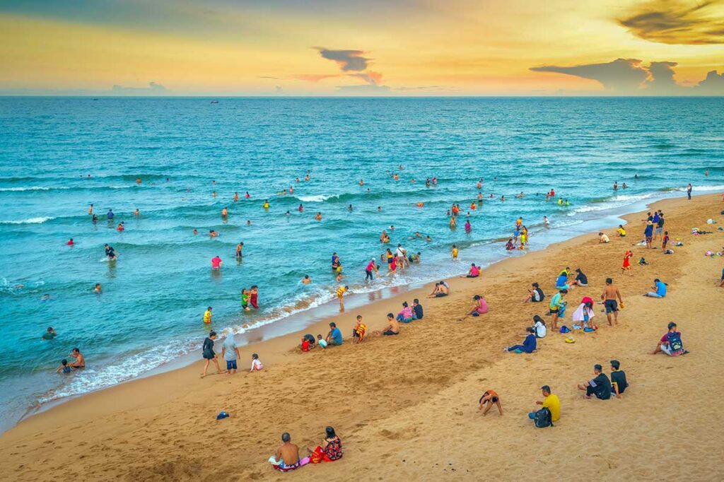 Crowds of locals swimming and relaxing at Tuy Hoa Beach during sunset in Phu Yen Province.