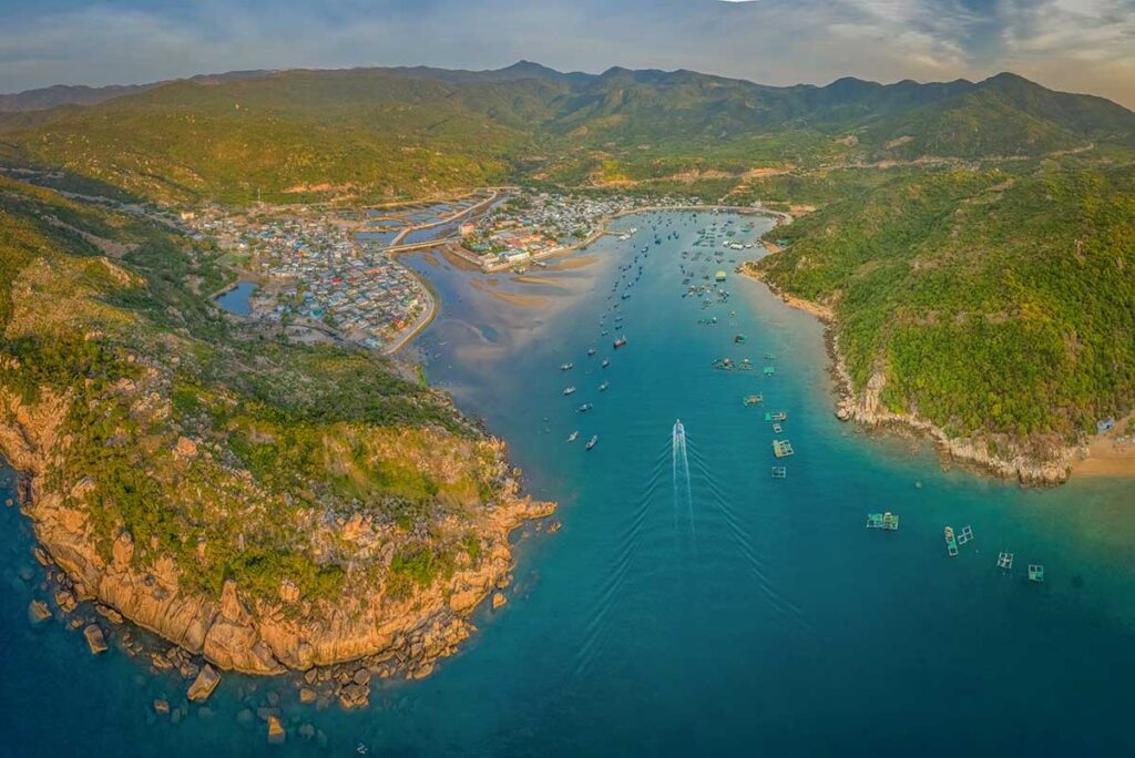 Aerial view of Vinh Hy Bay and fishing village – Drone view of the bay with floating seafood farms, sandy inlets, and the village nestled between rocky headlands and Nui Chua hills.
