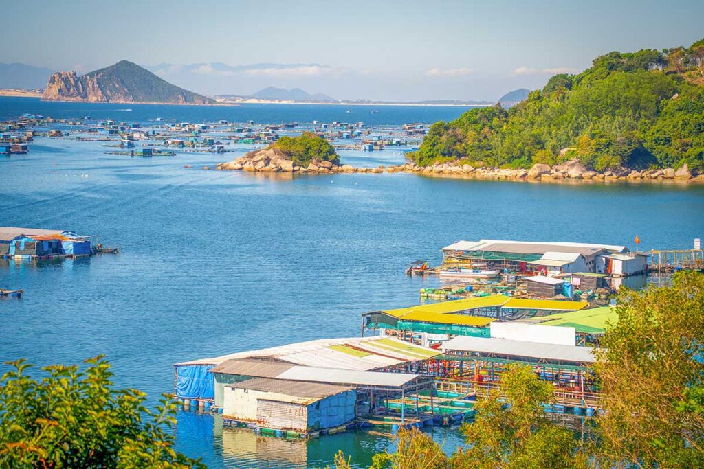 Cluster of floating houses and fish farms in Vung Ro Bay, with Hon Nua Islet visible in the distance.