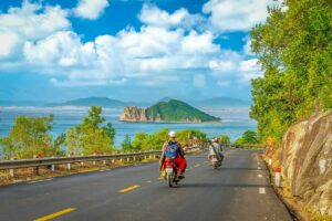 Motorcyclists riding along Ca Pass with a dramatic view of Hon Nua Islet and the blue sea below.