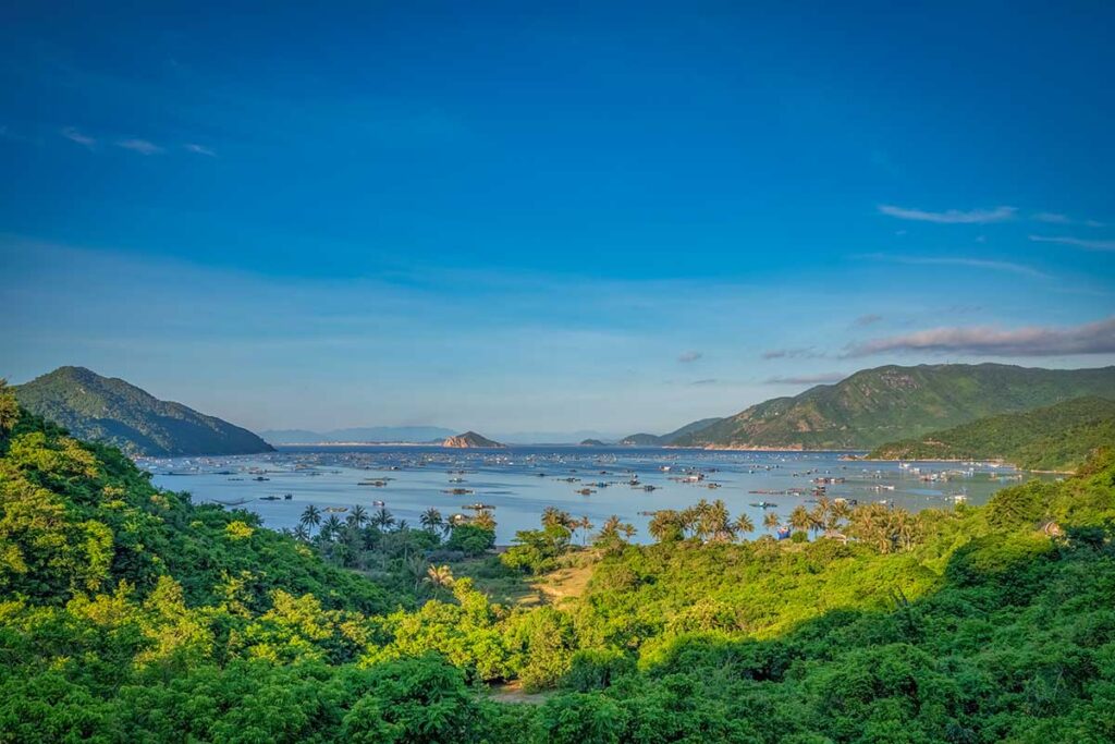 Viewpoint overlooking Vung Ro Bay with calm turquoise water, fishing boats, and green mountains under a clear sky.