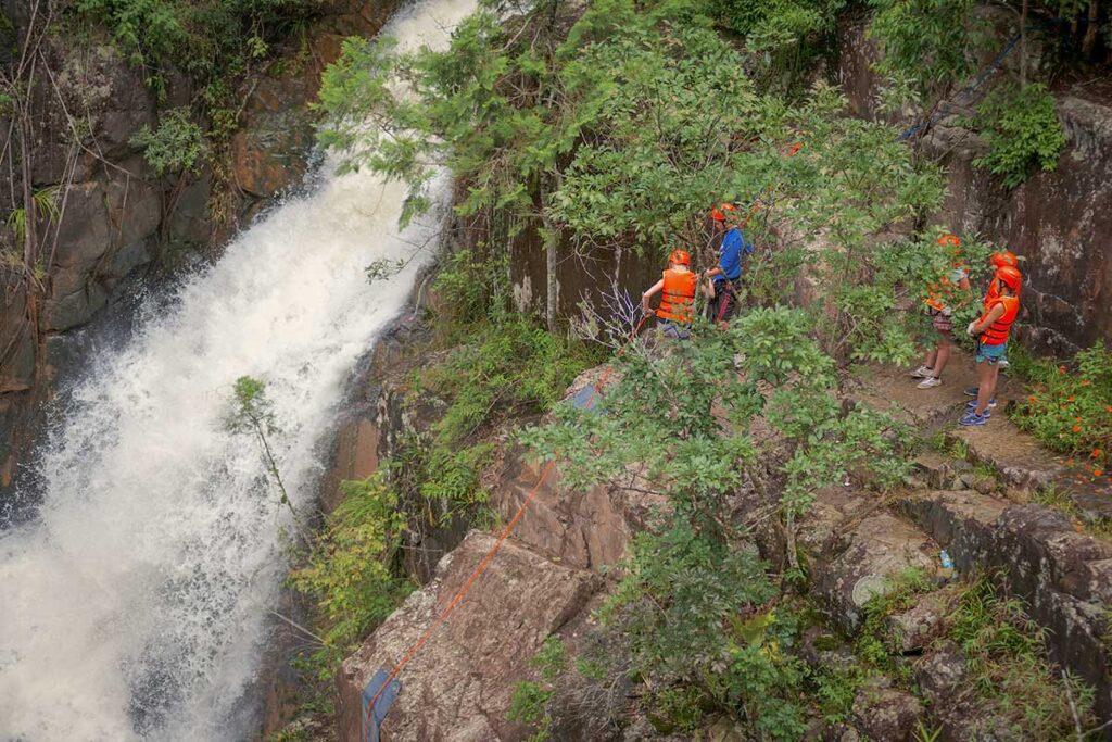Travelers canyoning down a waterfall in Dalat’s pine-covered highlands, a thrilling highlight of adventure tours in Central Vietnam.