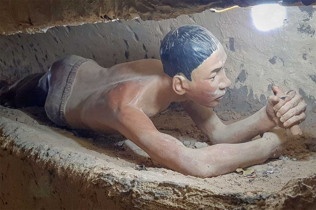 Wax figure of a prisoner crawling through a reconstructed escape tunnel at Phu Quoc Prison, showing the narrow earthen passage dug by prisoners during the Vietnam War.