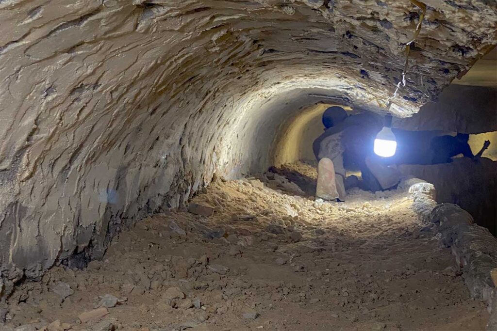 Narrow hand-dug escape tunnel inside Phu Quoc Prison, with rough earthen walls and a wax figure of a prisoner crawling through the darkness.