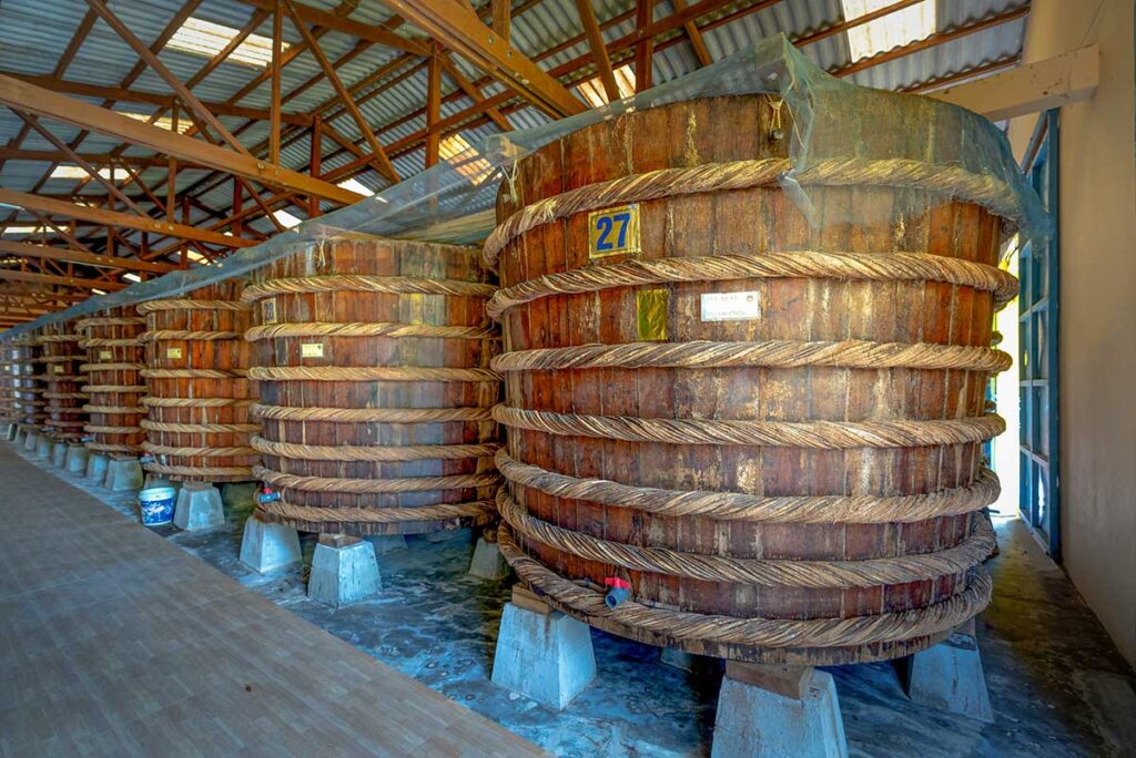 Long corridor of traditional wooden fermentation barrels at a Phu Quoc fish sauce factory, each barrel numbered and raised on concrete blocks