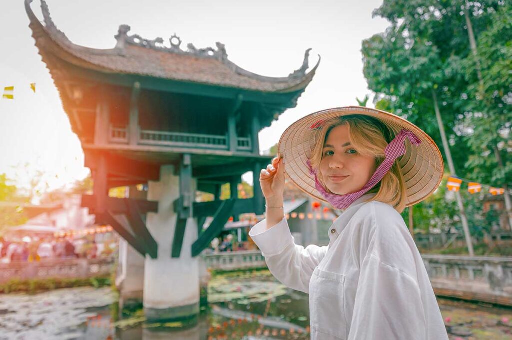 Hanoi tours visiting the One Pillar Pagoda with a traveler wearing a conical hat in the temple courtyard