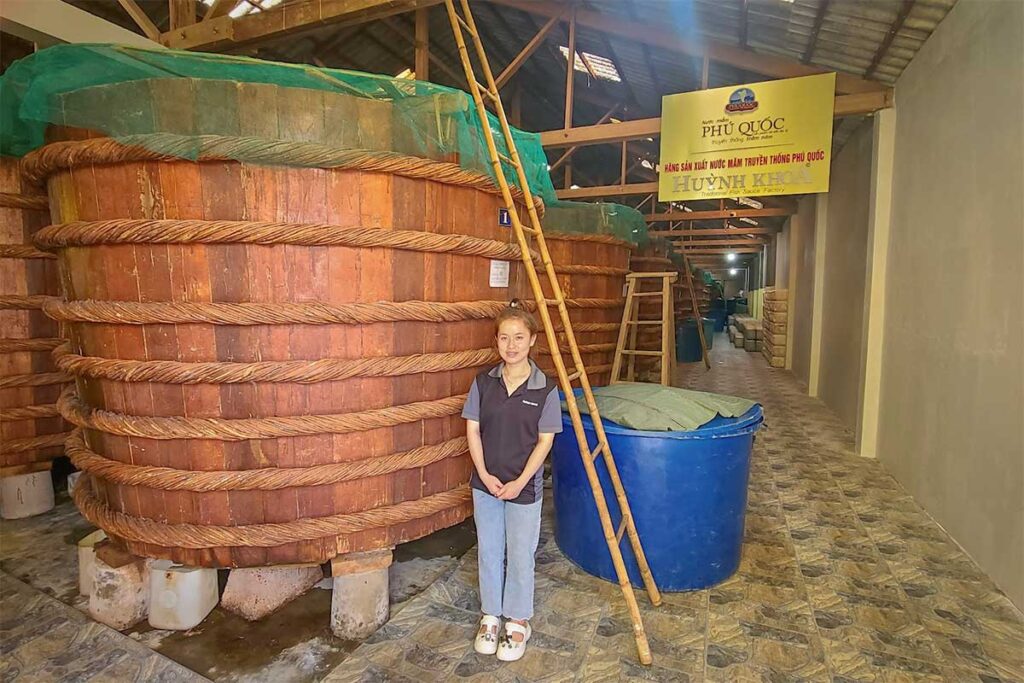 Staff member standing next to a large traditional fermentation barrel at Huynh Khoa fish sauce factory in Phu Quoc