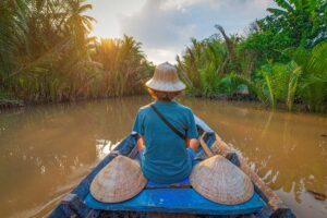 Traveler on a traditional wooden boat through palm-lined canals of the Mekong Delta — a serene experience included in southern Vietnam tours.