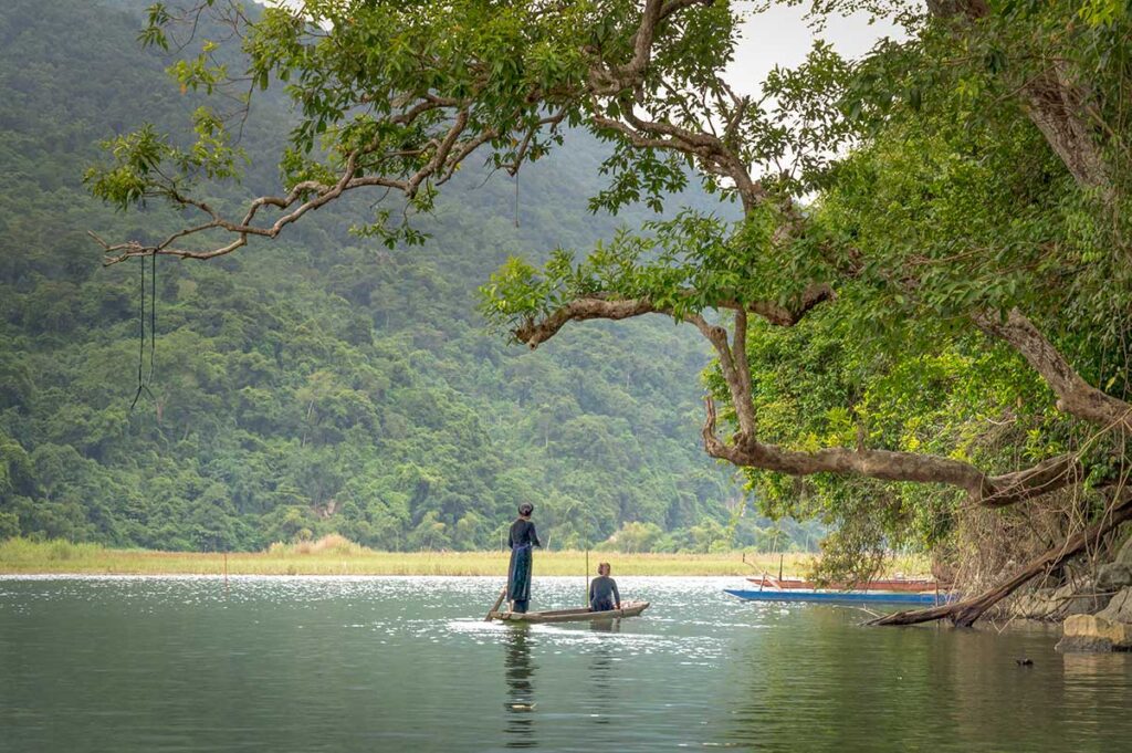 Locals paddling a wooden boat on Ba Be Lake surrounded by dense jungle, a serene destination on nature-focused North Vietnam tours.
