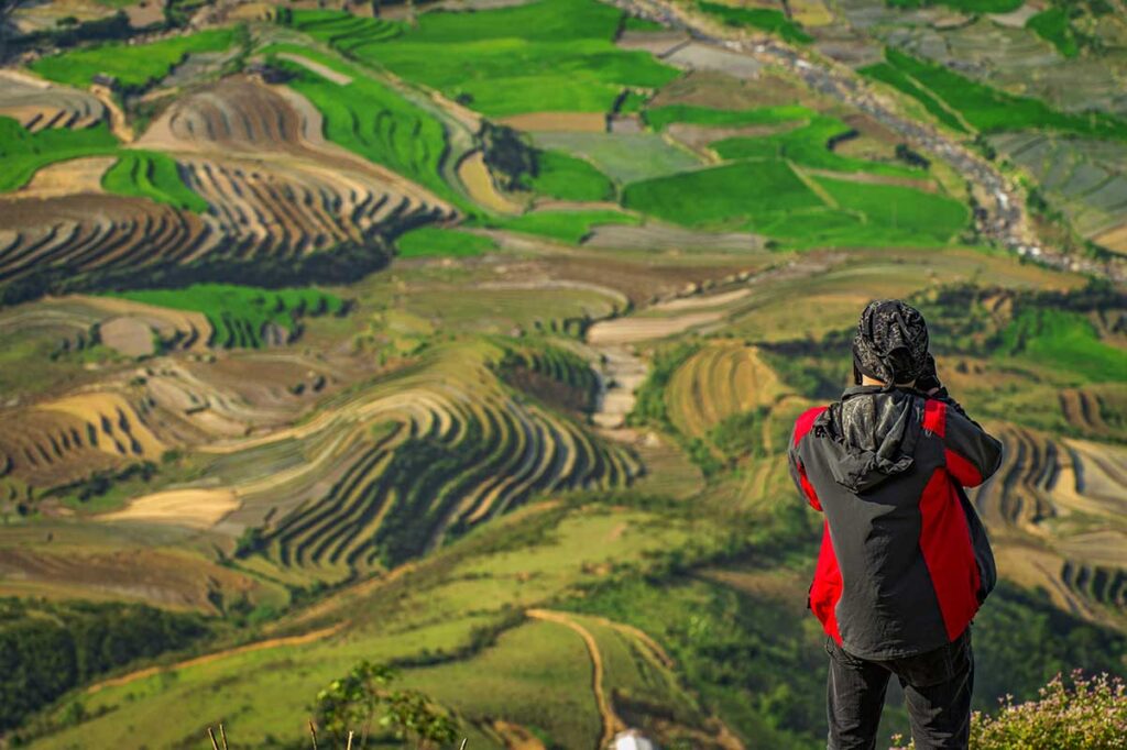 Traveler photographing layered rice terraces in Mu Cang Chai, a photographer’s favorite on Northern Vietnam adventure tours.