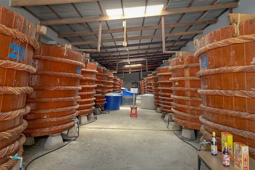 Fermentation barrels at Phung Hung fish sauce factory in Phu Quoc, with smaller collection containers visible between the wooden vats