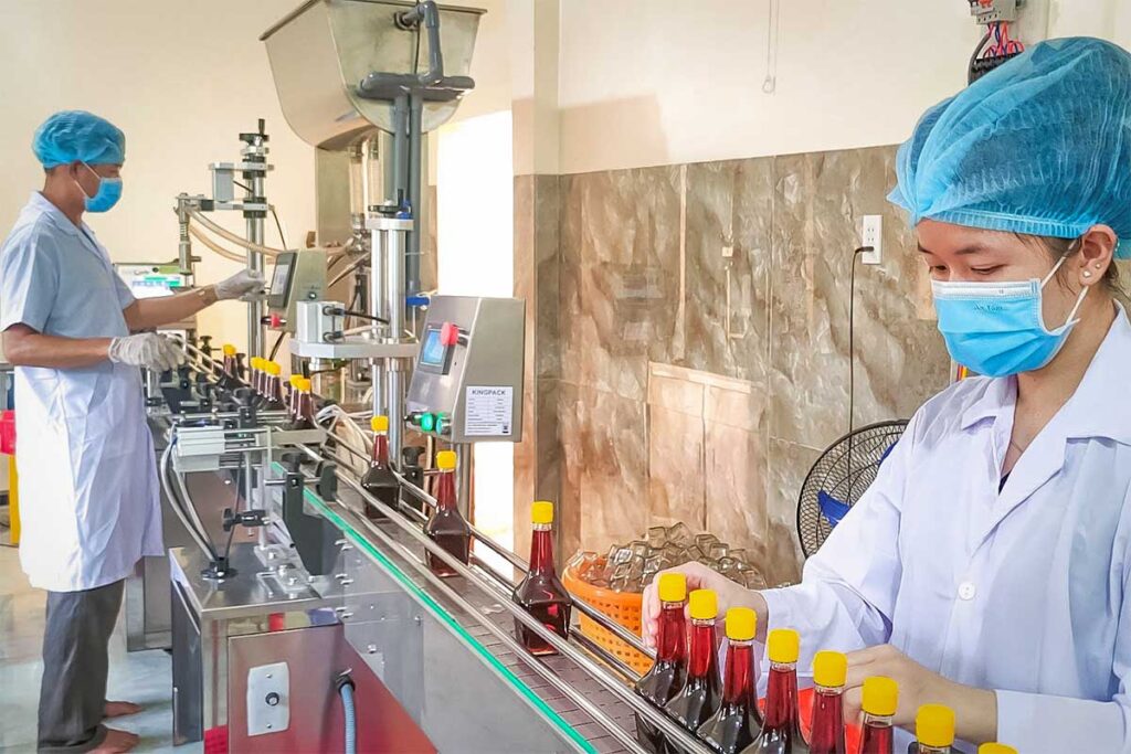 Workers in protective clothing bottling fish sauce on a production line at a Phu Quoc fish sauce factory