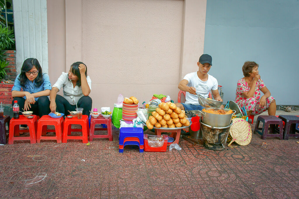 Locals enjoying traditional street food on plastic stools during an evening Ho Chi Minh City street food tour in South Vietnam.