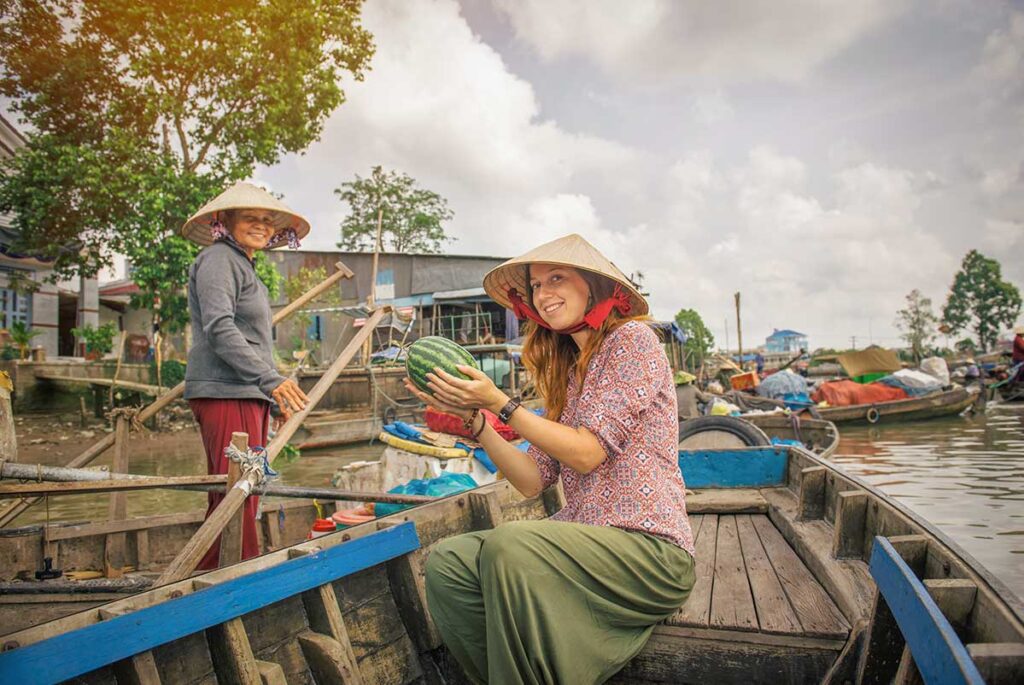 Local guide and traveler on a wooden boat at the floating markets of the Mekong Delta during a Southern Vietnam tour.