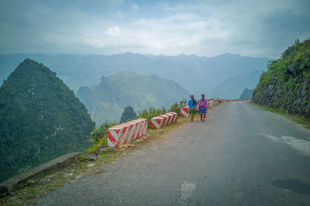 Ethnic women walking along a mountain road in Ha Giang with dramatic limestone peaks – a scenic stop on a Vietnam package tour.