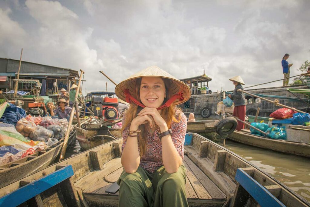 Traveler wearing a conical hat on a wooden boat at a floating market in the Mekong Delta – a classic experience on a southern Vietnam package tour.