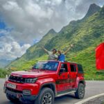 Guests standing through the open roof of a red jeep during a Ha Giang Loop jeep tour with Local Vietnam, captured on an actual mountain road stop surrounded by dramatic limestone scenery.