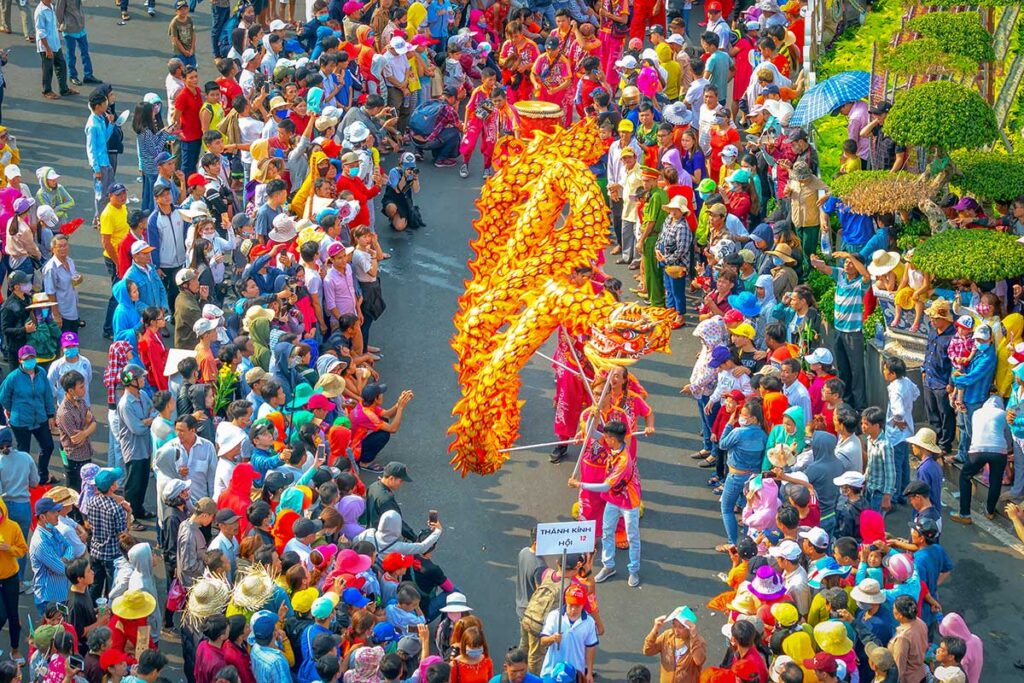 Vietnamese dragon dance performance during a large public festival, with a long dragon costume moving through a crowded street surrounded by spectators.