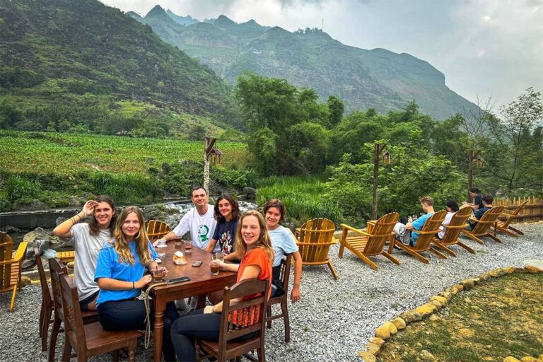 Local Vietnam guests relaxing during a Ha Giang Loop tour stop in Du Gia, sitting by the river with mountain views after a day of traveling by jeep and car through northern Vietnam