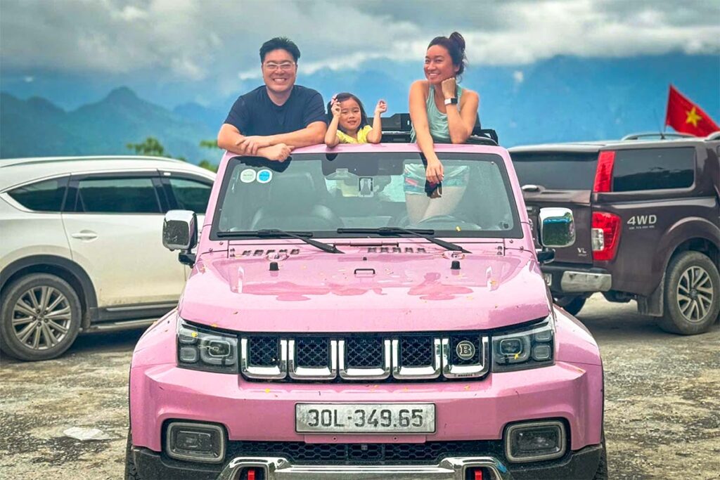 Ha Giang Loop jeep tour by Local Vietnam, showing a guest sitting on the roof of a pink jeep parked at a mountain pass viewpoint