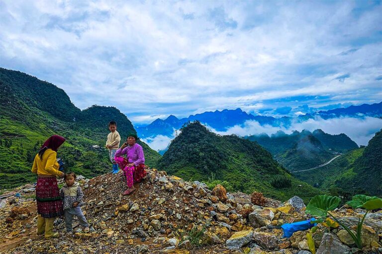 Ethnic minority family in a mountain landscape along the Ha Giang Loop, with panoramic views over valleys and winding roads