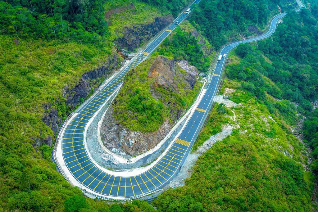Aerial view of a dramatic hairpin bend on Khanh Le Pass, surrounded by dense forest and steep mountain slopes