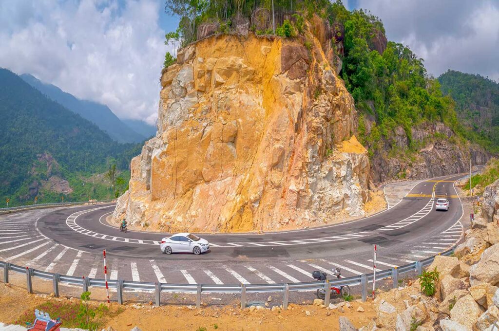 Cars navigating a tight mountain curve on Khanh Le Pass, illustrating the dramatic road engineering through steep rocky terrain
