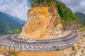 Cars navigating a tight mountain curve on Khanh Le Pass, illustrating the dramatic road engineering through steep rocky terrain