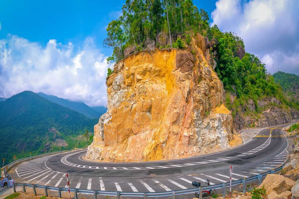 Sharp hairpin bend on Khanh Le Pass with rocky cliffs and a parked motorbike, a popular photo stop on the Dalat to Nha Trang journey