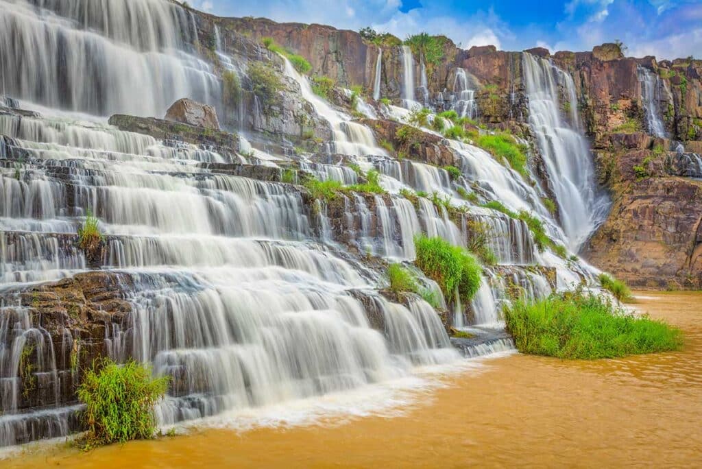 Wide-angle view of Pongour Waterfall near Dalat with powerful water streams flowing across stepped rock formations.