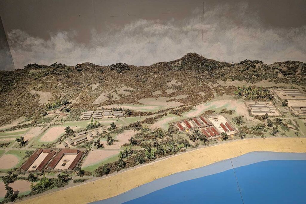 Detailed scale model of the Con Dao prison system along the coastline, showing layout of prison camps and surrounding landscape.