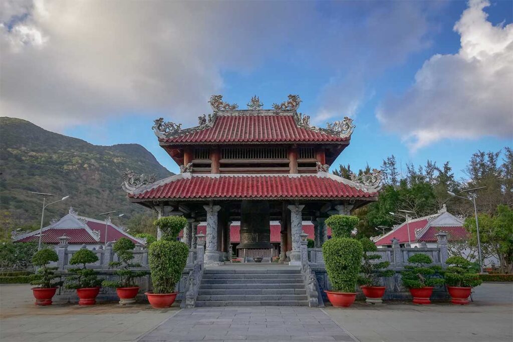 Temple building with a large bronze bell inside Hang Duong Cemetery in Con Dao, used for ceremonies and offerings by visitors.