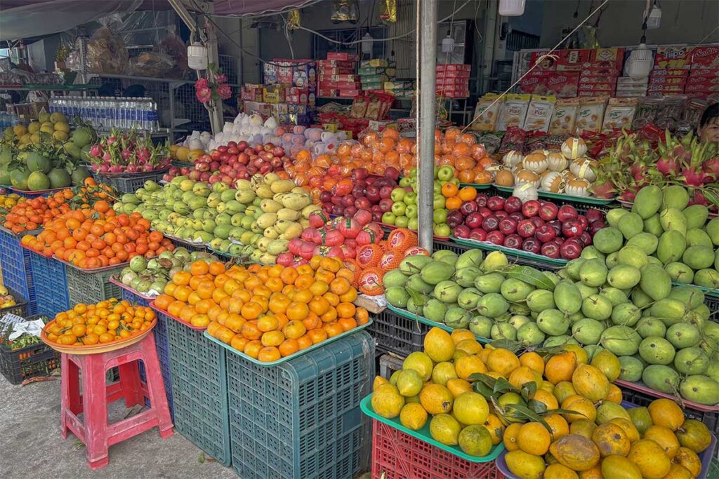 Colorful fruit stall at Con Dao Market displaying fresh tropical fruits like mango, oranges, dragon fruit and apples in the daytime market