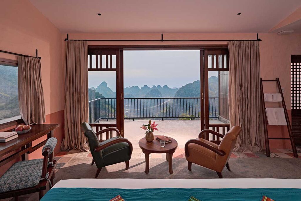 Bungalow room at Ha Giang Aya Lodge with large window and balcony overlooking the mountains of the Dong Van Karst Plateau.
