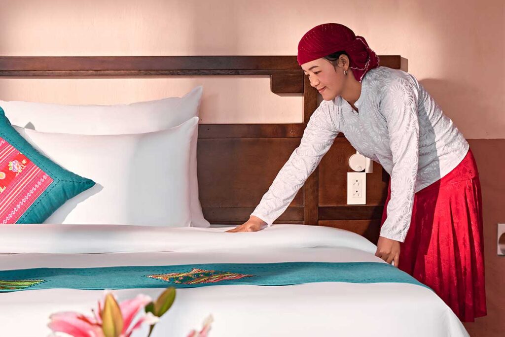 Hmong staff member preparing a bed in a guest room at Ha Giang Aya Lodge along the Ha Giang Loop.