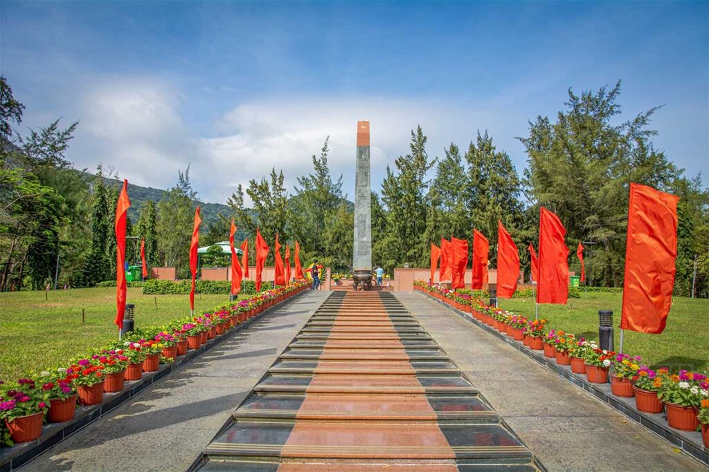 Main memorial monument at Hang Duong Cemetery with red flags lining the path, honoring fallen prisoners on Con Dao island.