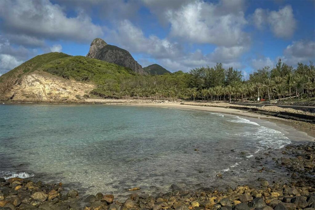 Quiet beach at Orson Hotel & Resort Con Dao with clear water, rocky shoreline, and mountains in the background