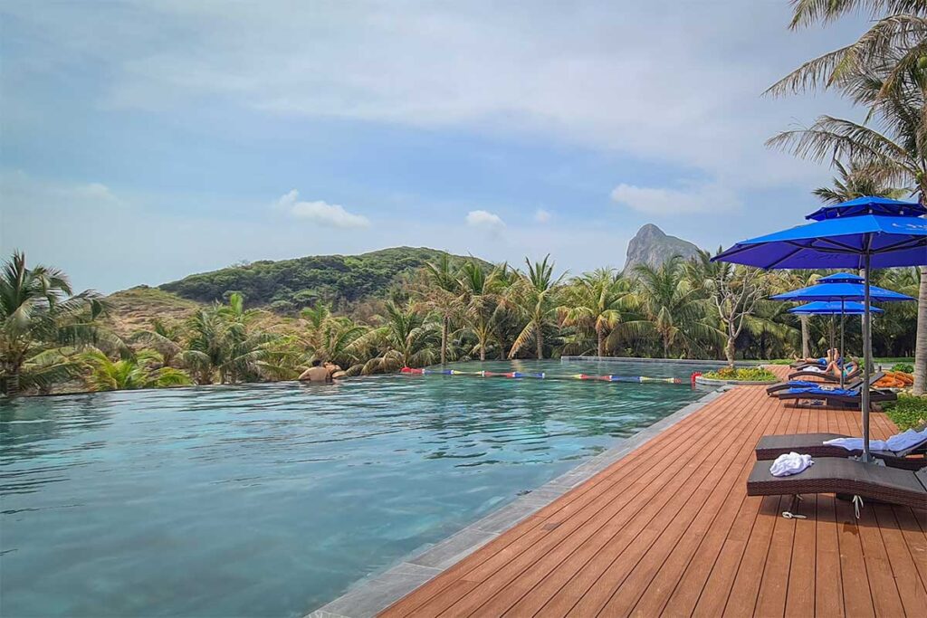 Infinity pool at Orson Hotel & Resort Con Dao surrounded by palm trees, sun loungers, and views of the island hills