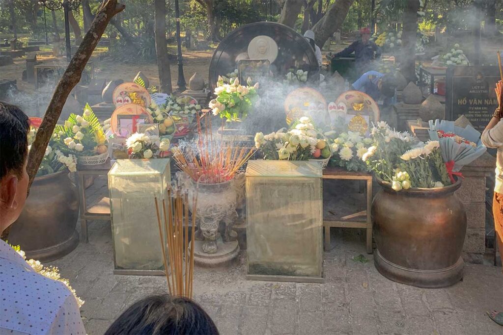 Incense burning and offerings placed at Vo Thi Sau grave during the day, with visitors paying respect at Hang Duong Cemetery in Con Dao.