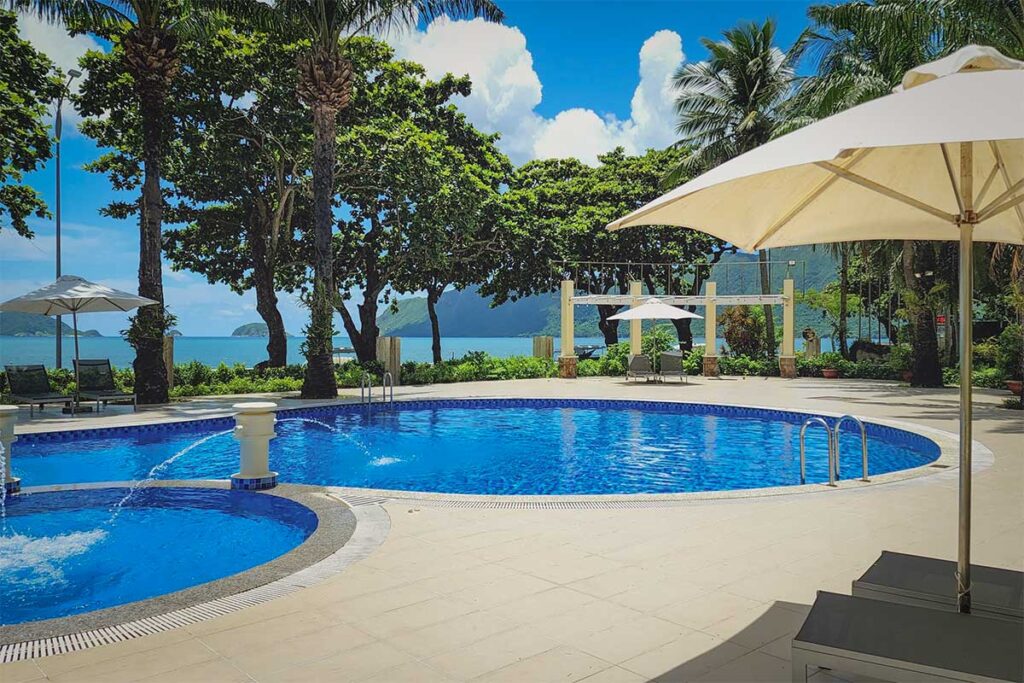 Swimming pool at Sai Gon Con Dao Resort with sun umbrellas, palm trees, and ocean view in the background