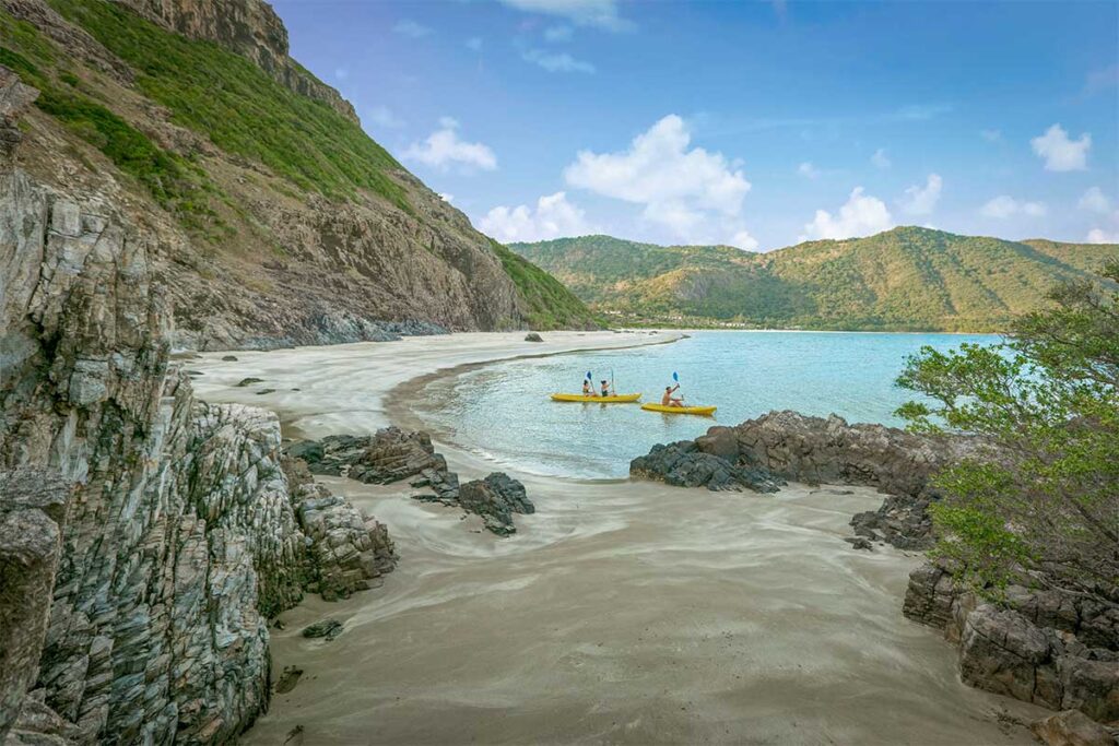 Quiet bay at Six Senses Con Dao with white sandy beach, clear water, and people kayaking along the coastline