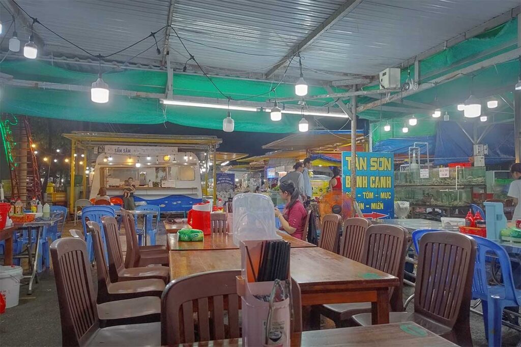 Street food stalls at Con Dao night market with plastic tables and chairs, where visitors enjoy fresh seafood and local dishes in a casual evening setting