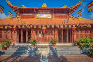 Front view of the main temple building at Van Son Pagoda in Con Dao with wooden architecture, red lanterns and Buddhist flags