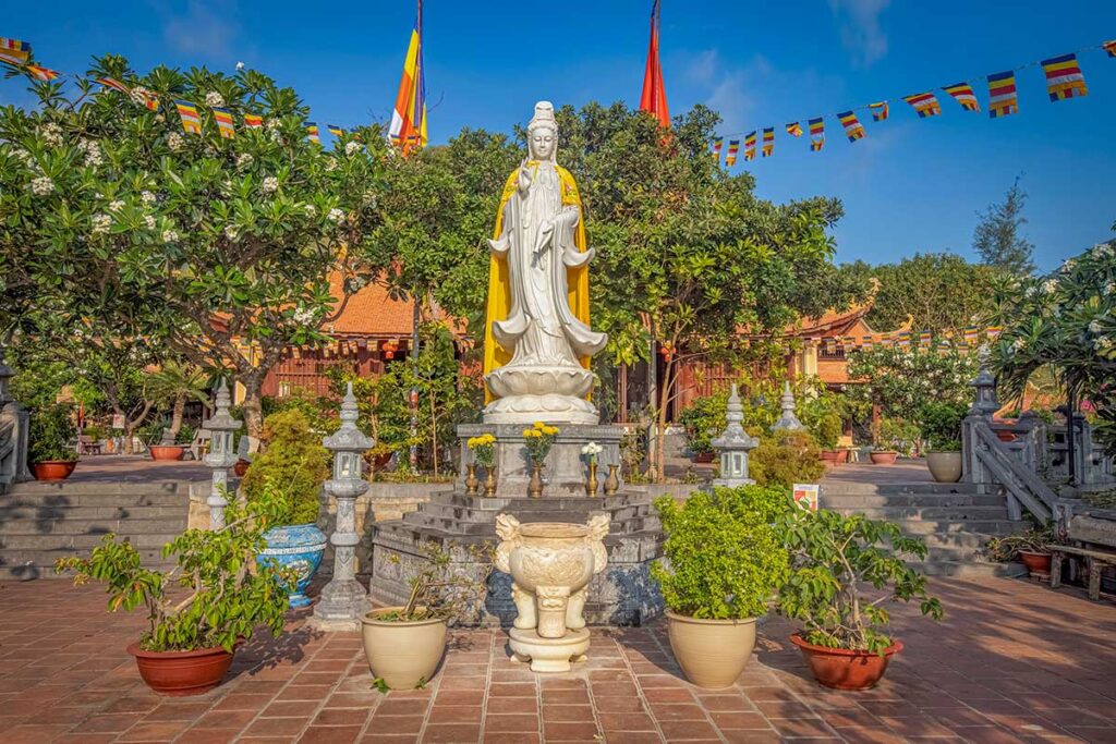 Quan Am statue in the courtyard of Van Son Pagoda in Con Dao, surrounded by plants and temple buildings