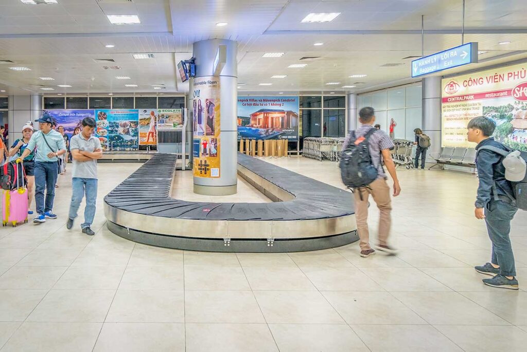 Baggage claim area at Cam Ranh Airport with luggage belt and travelers waiting for their suitcases after arrival