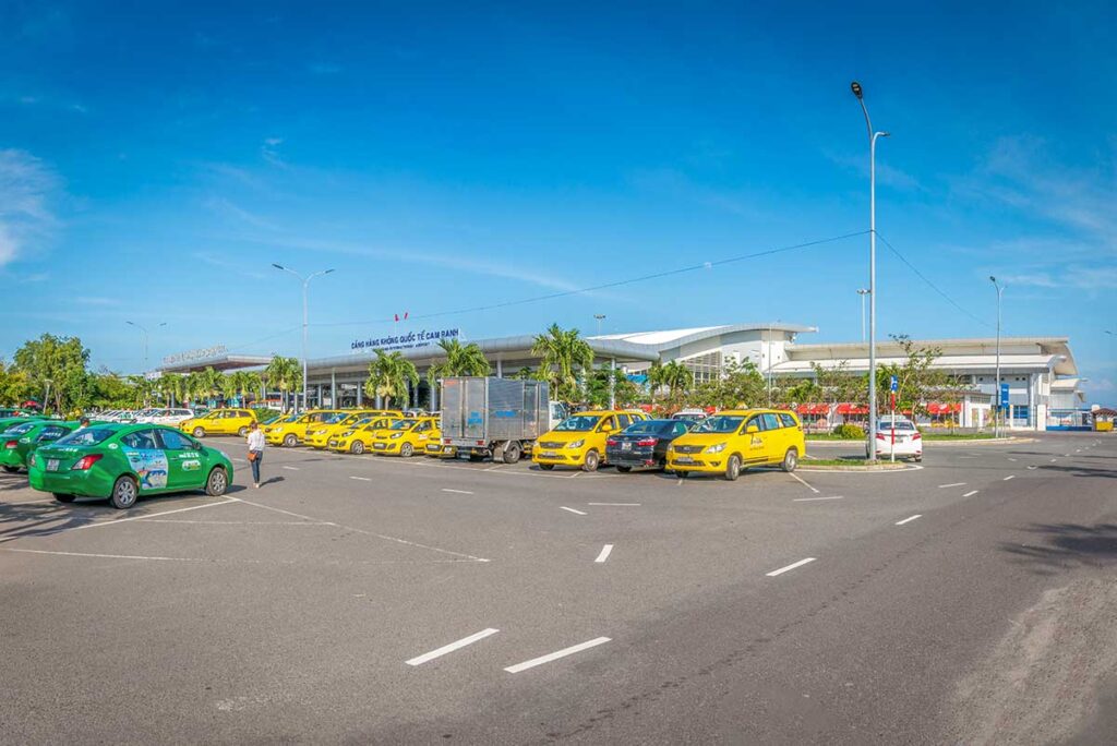 Taxi pickup area outside Cam Ranh Airport with multiple cars waiting to take passengers to Nha Trang and nearby resorts