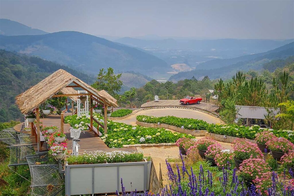 Scenic viewpoint with flowers and a small wooden structure at Cao Nguyen Hoa, overlooking the valley near the Dalat Flower Plateau Ecotourism Area