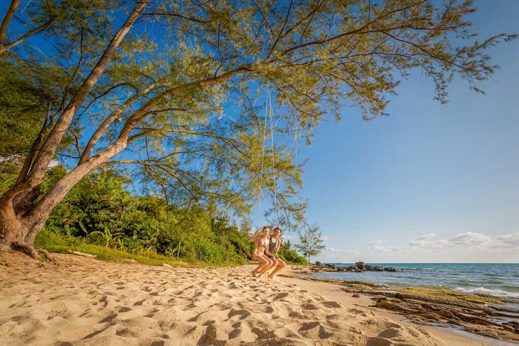 Couple on swing at Cua Can Beach Phu Quoc with sandy shore sea view and tropical trees