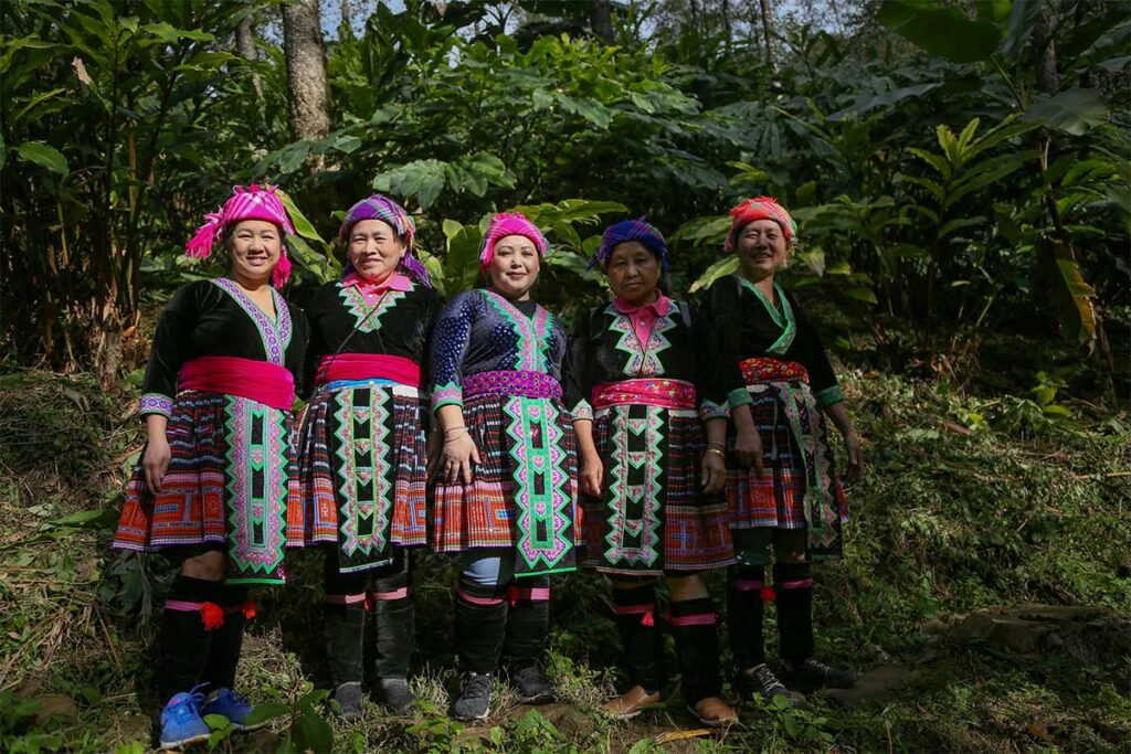 Group of Hmong women wearing colorful traditional clothing in Sin Suoi Ho village surrounded by forest